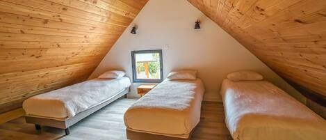 A cozy attic bedroom with wooden walls and sloped ceilings, featuring two single beds and a small table.