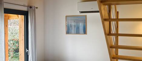 Une chambre à coucher avec un lit, un escalier en bois, un tableau et une fenêtre avec des rideaux.