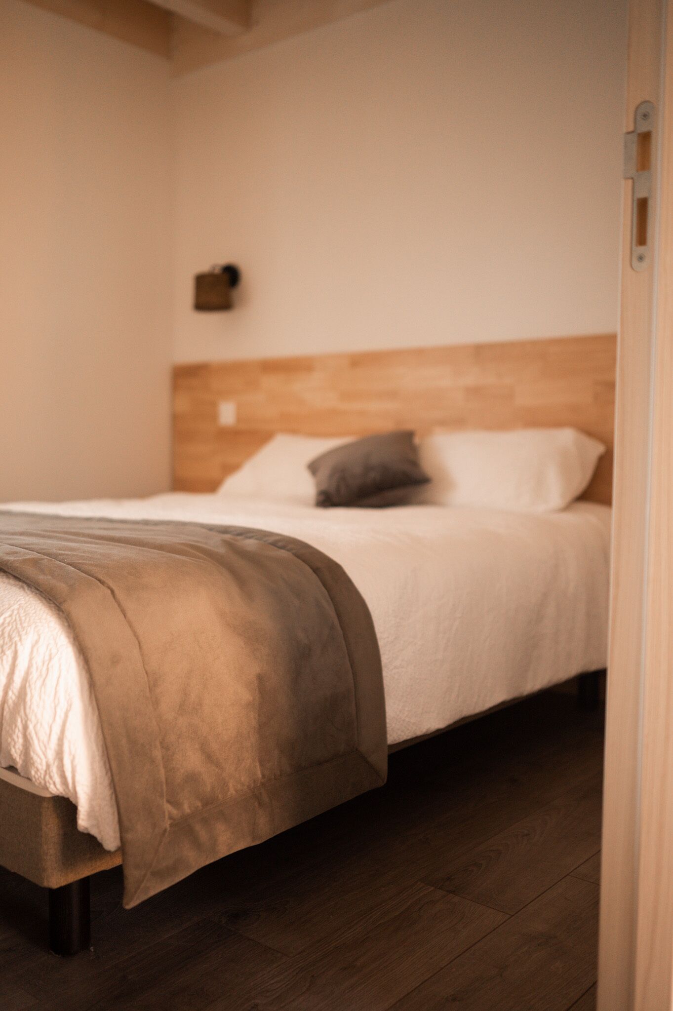 Una cama bien hecha con cabecera de madera, una manta marrón y una mesita de noche con una lámpara.
