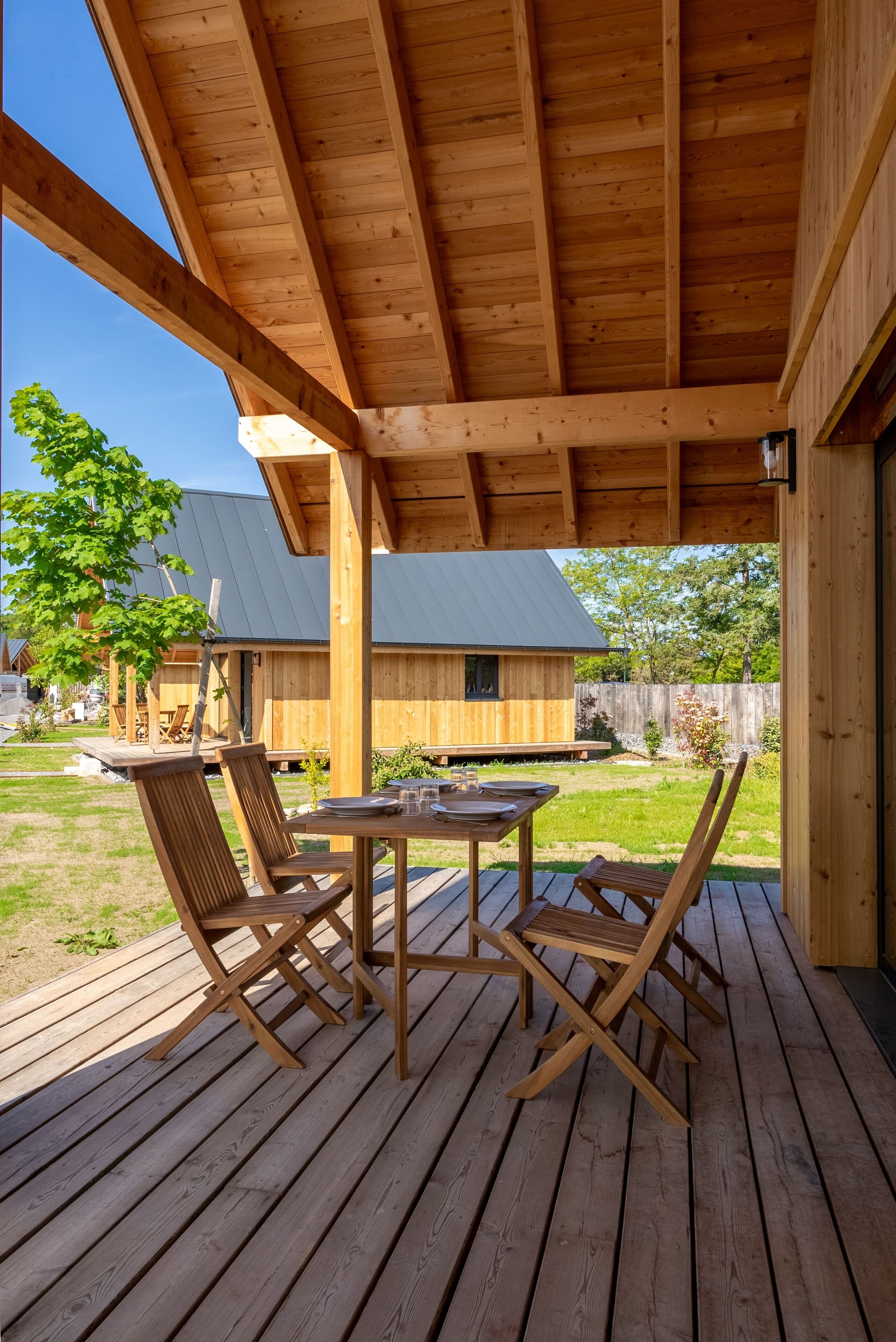 A wooden deck with a table and chairs, a covered area with a wooden ceiling, and a view of a house in the background.
