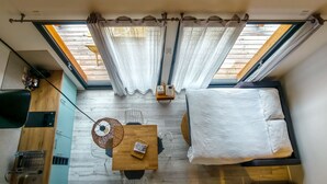 Una habitación compacta con suelo de madera, una mesita con una cesta, una silla, un sofá y una cama.