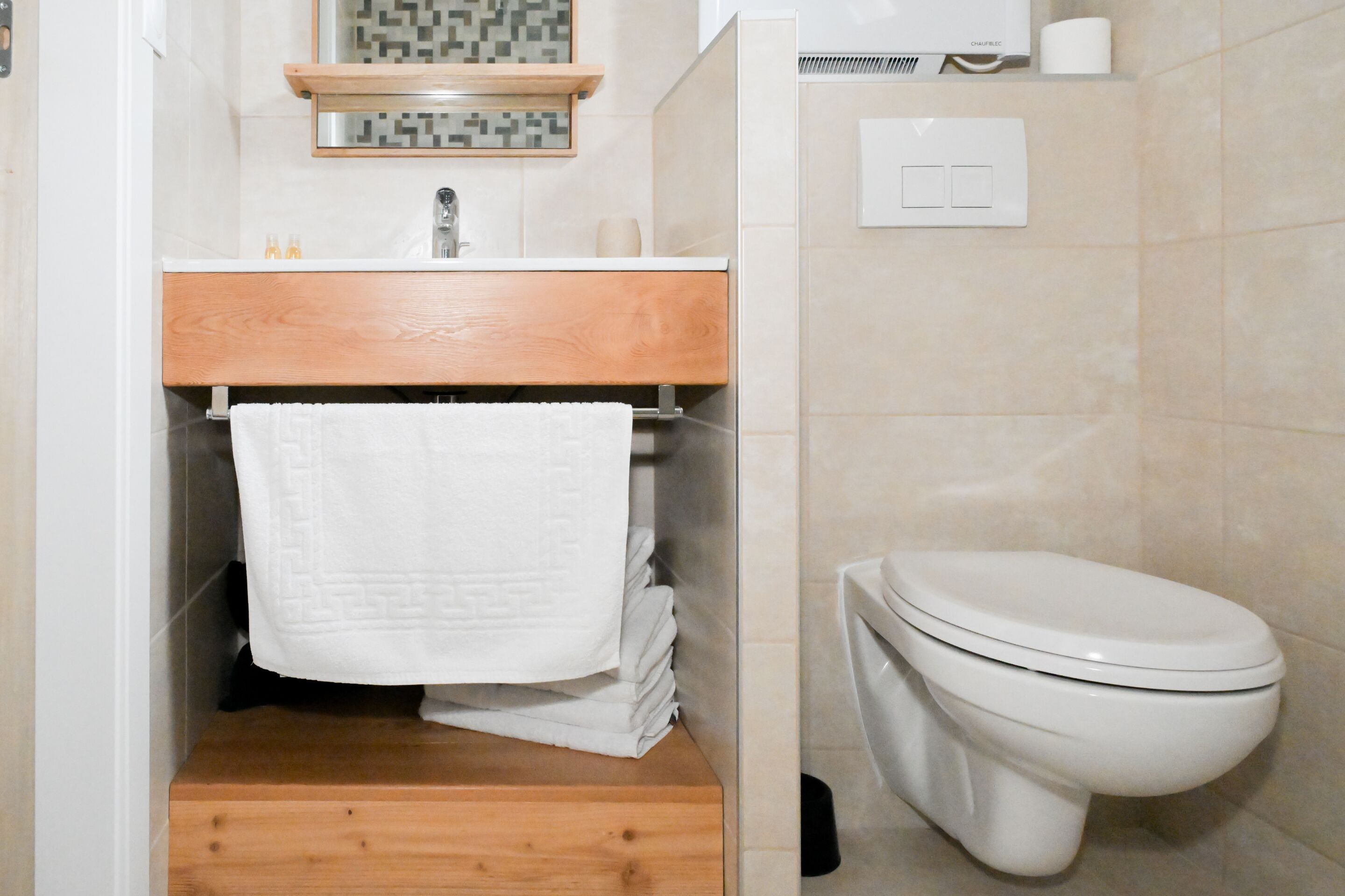 A bathroom with a wooden vanity, a toilet, and a tiled wall.
