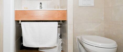 Un baño con tocador de madera, inodoro y pared con azulejos.