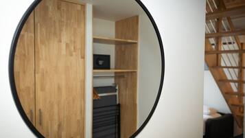 Un miroir rond reflète une pièce avec des meubles en bois, une étagère noire et un escalier avec des rampes en bois.