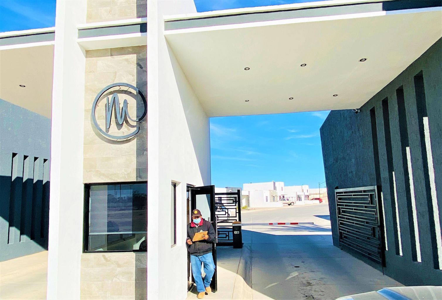 A modern building entrance with a large logo, a glass door, and a metal gate.