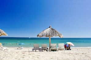A beach with lounge chairs and a thatched umbrella. - STUNNING 3 BED HOME - 2 POOLS - GATED COMMUNITY- CLOSE TO SANDY BEACH (Puerto Peñasco)