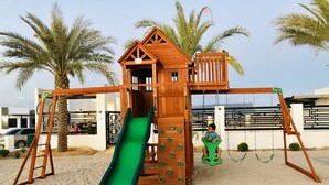 Ein hölzerner Spielplatz mit Rutsche, Kletterwand und Schaukeln.