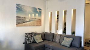 Ein modernes Wohnzimmer mit einem grauen Ecksofa, einem großen Landschaftsbild und mehreren vertikalen Lampen.