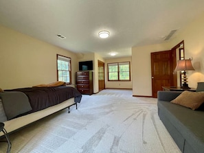 A spacious room with a large bed, a desk, and a chair. There are two windows and a door.