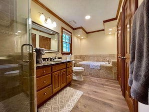 A bathroom with a glass shower enclosure, wooden vanity, a bathtub, and a toilet.