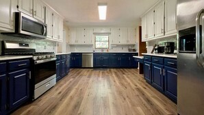 Eine geräumige Küche mit dunkelblauen Schränken, einem Edelstahlkühlschrank und Holzboden.