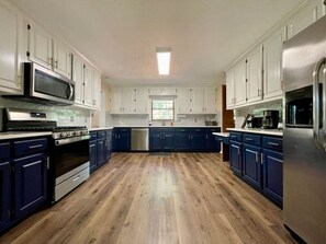 A spacious kitchen with dark blue cabinets, a stainless steel refrigerator, and a wood floor.