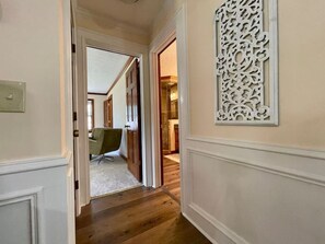 A hallway with wooden flooring, white walls, and a decorative panel.