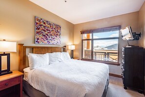 Une chambre d’hôtel avec un grand lit, deux tables de chevet, un bureau, une chaise, une fenêtre donnant sur un beau paysage et un téléviseur posé sur un meuble.