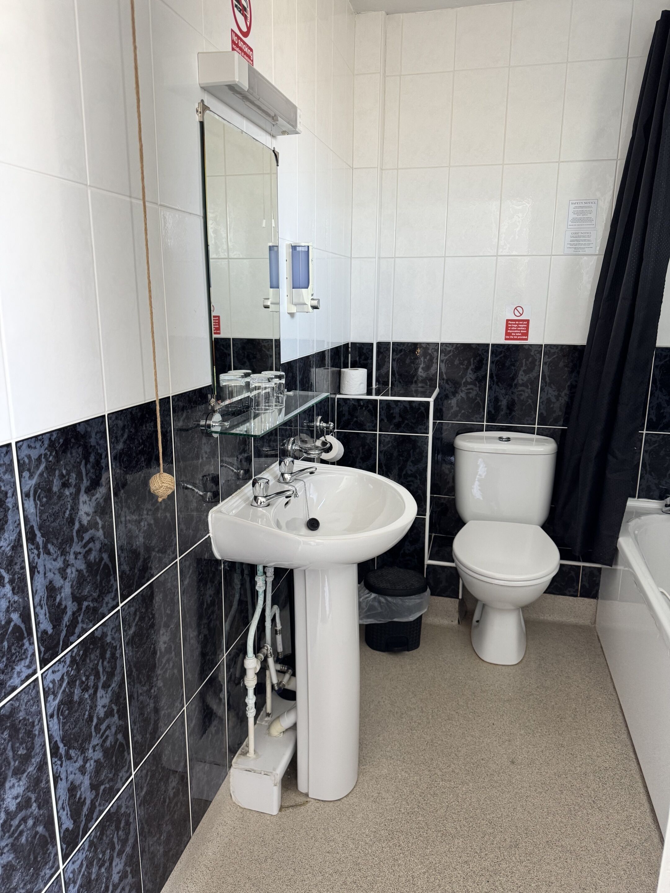 A bathroom with a white sink, toilet, and bathtub. There is a mirror above the sink and a hand dryer on the wall.