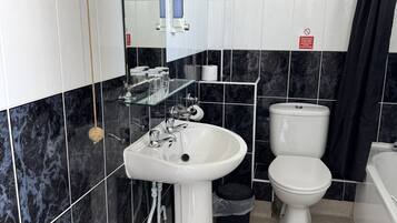 A bathroom with a white sink, toilet, and bathtub. There is a mirror above the sink and a hand dryer on the wall.