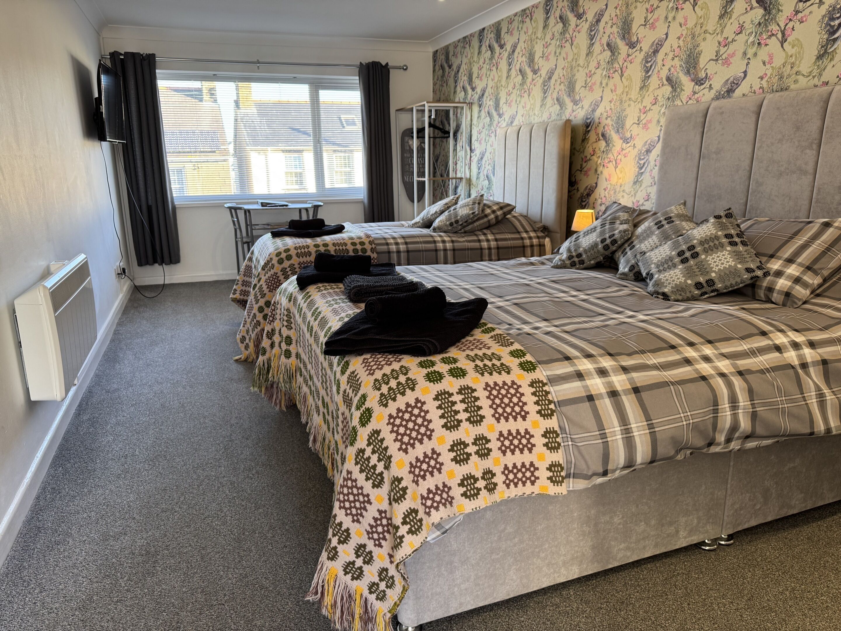 A hotel room with two beds, a radiator, a television, and a window with curtains.