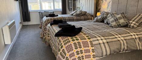 A hotel room with two beds, a radiator, a television, and a window with curtains.