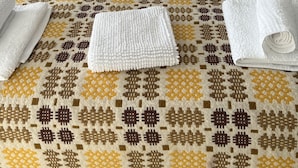 A neatly made bed with a patterned bedspread, pillows, and folded towels. - Traeth Rooms (Cardigan)