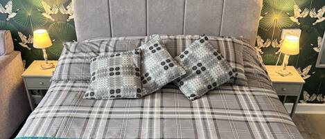 A neatly made bed with a plaid bedspread, two pillows with a geometric pattern, and a folded towel on a green textured blanket.