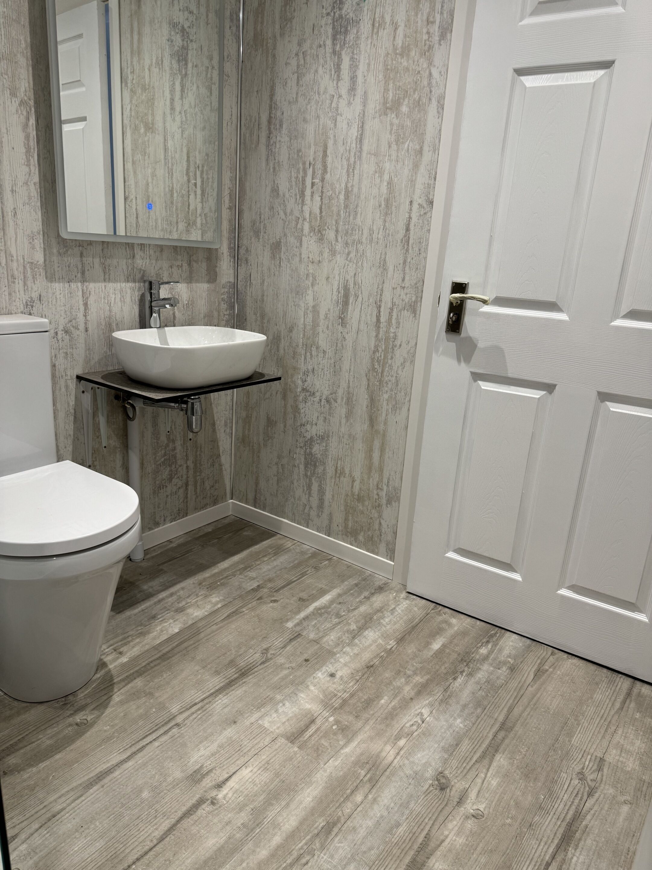 Ein Badezimmer mit einer weißen Toilette, einem weißen Waschbecken auf einem schwarzen Regal und einem Holzboden.
