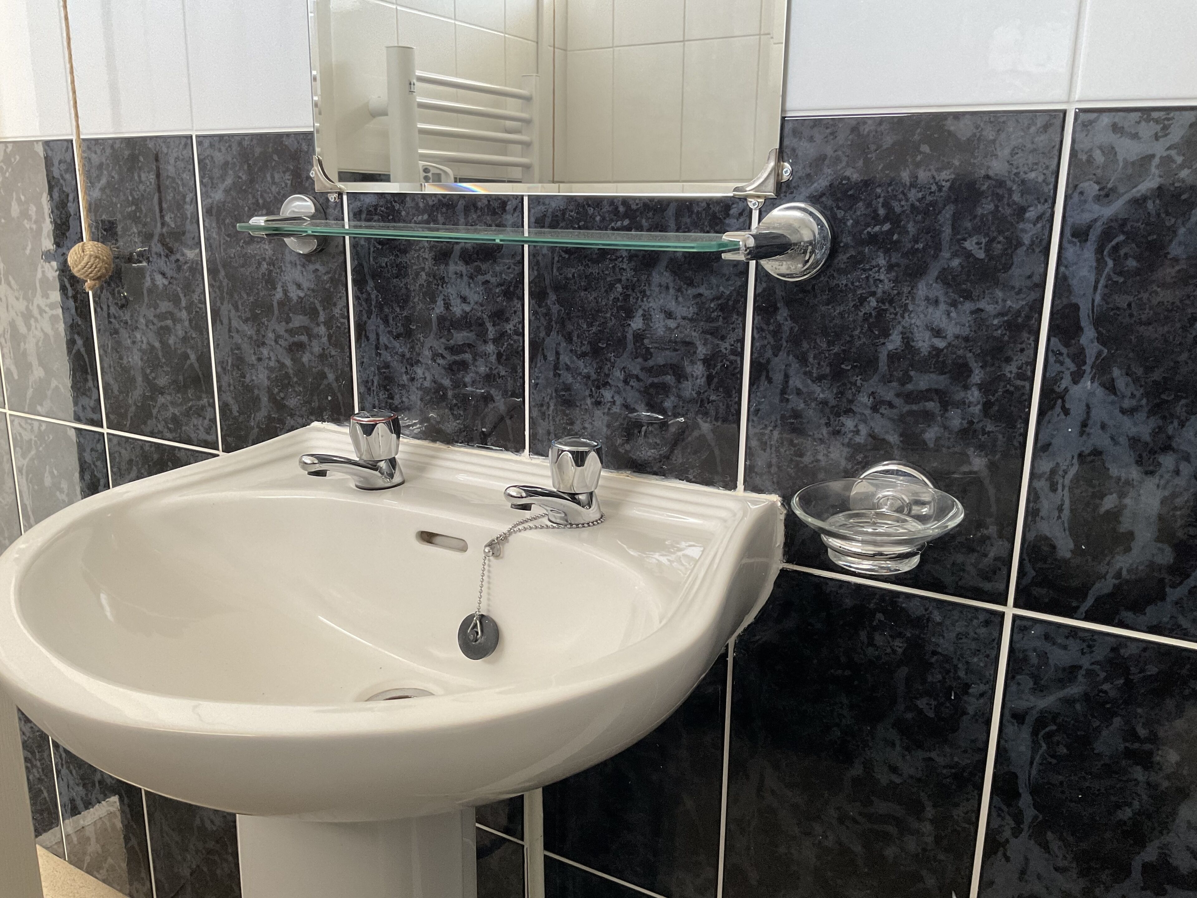 A bathroom with a white sink, black marble tiles, and a glass shelf.