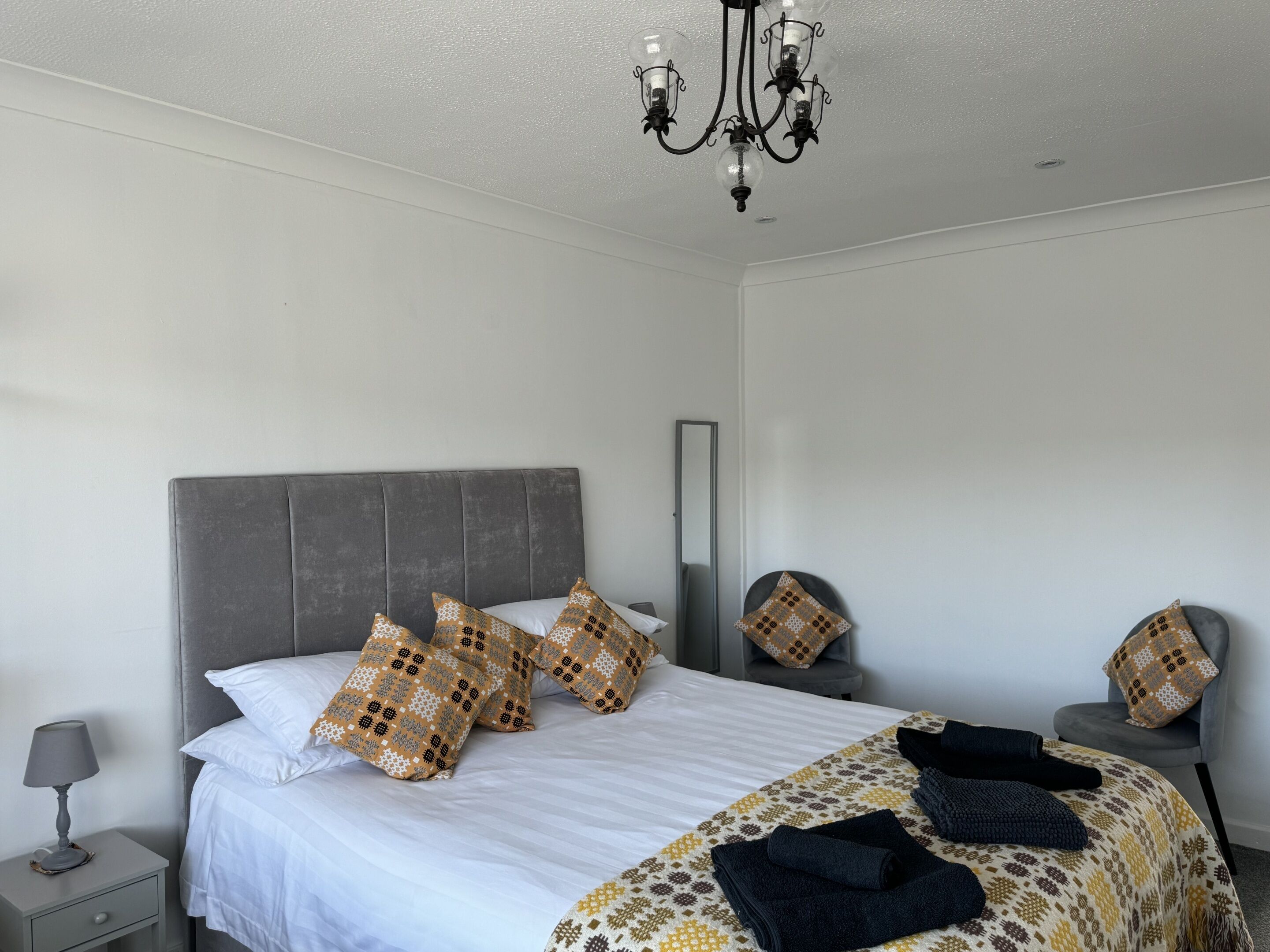 A neatly made bed with patterned pillows, a bedside lamp, and a folded towel on a patterned bedspread.