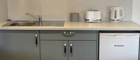 A kitchen with a stainless steel sink, a white coffee maker, and a white electric kettle on the countertop.