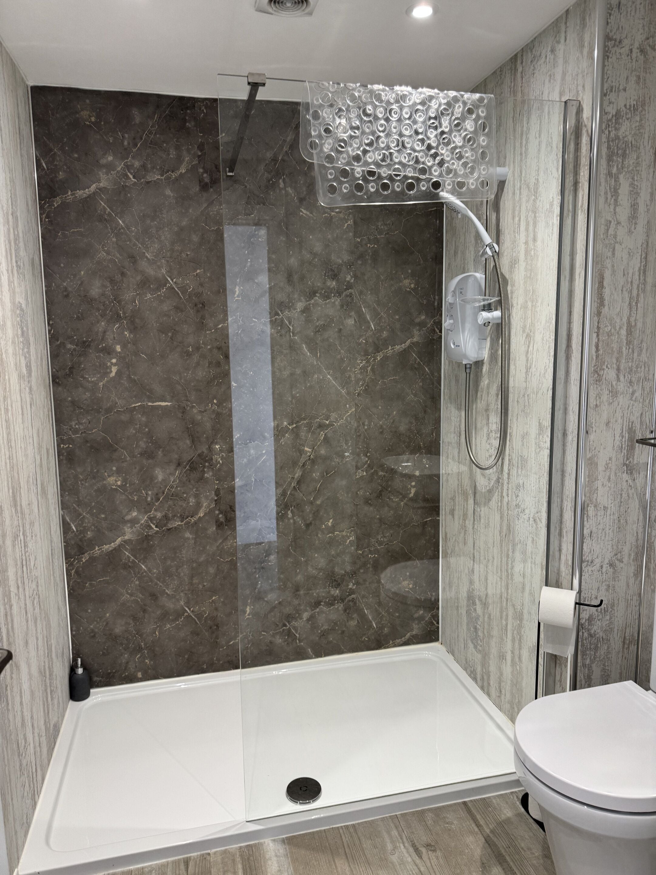 Een moderne badkamer met een douchecabine van glas, een wit toilet en een marmeren wand.