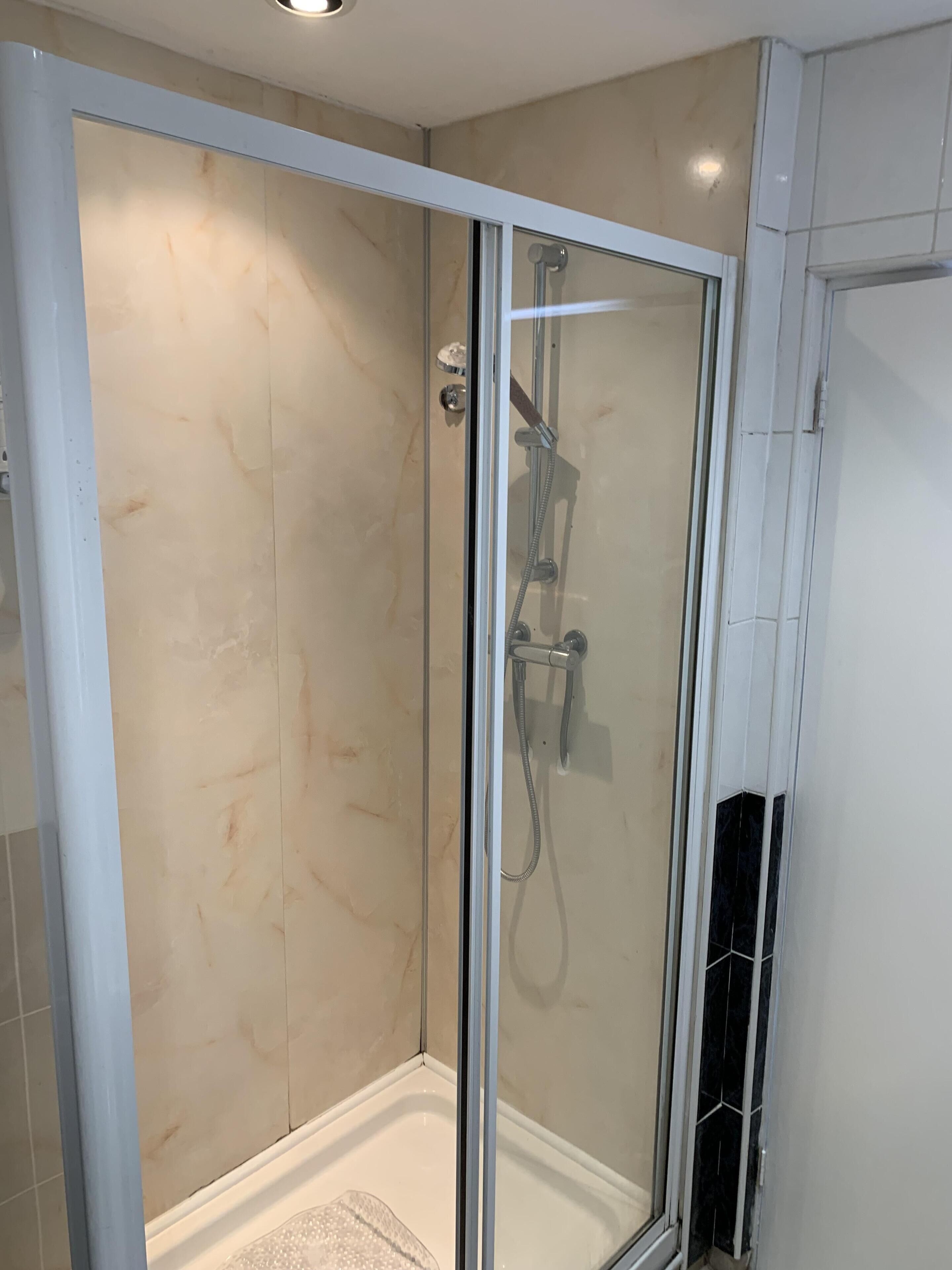 A glass-enclosed shower with a handheld showerhead and a fixed wall-mounted faucet.
