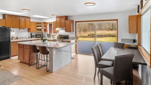 A modern kitchen with wooden cabinets, granite countertops, and a large island with bar stools. - Rainier Estates' 5 Acre, 3100sqft, HotTub, Events (Elbe)