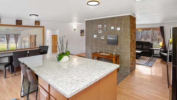 A modern kitchen with a granite island, wooden cabinets, and a dining area with a large window. - Rainier Estates' 5 Acre, 3100sqft, HotTub, Events (Elbe)