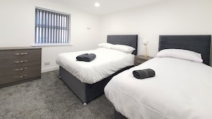 A hotel room with two beds, a dresser, and a window with blinds. - Dysa Banks Apartments (Blackpool)