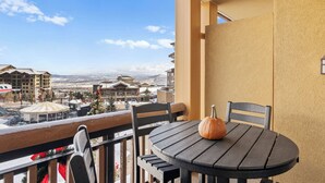 Un balcon avec une table et des chaises, une citrouille posée sur la table, et une vue sur des bâtiments et des montagnes en arrière-plan.