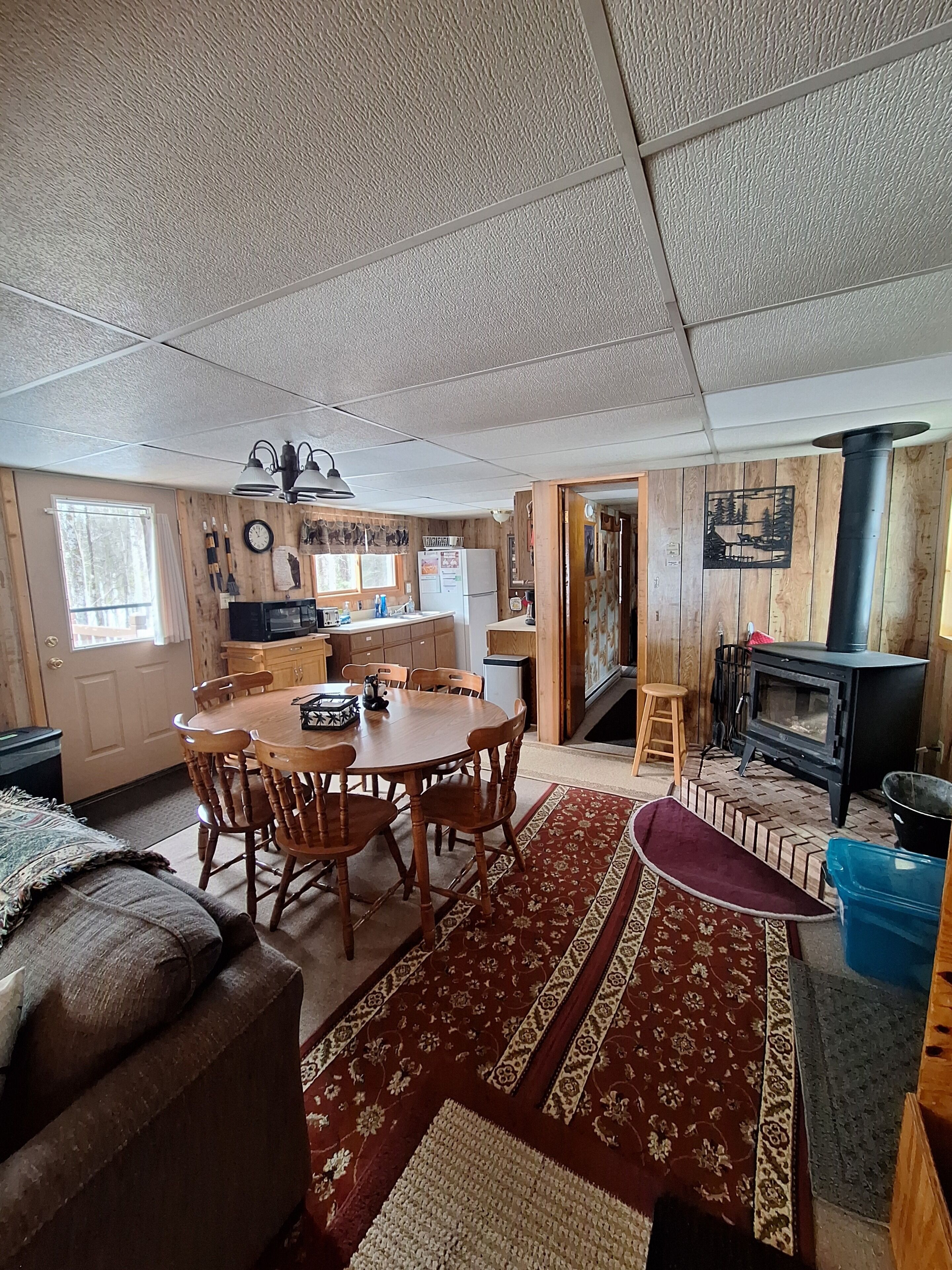 A cozy cabin interior with a dining area, kitchen, and a wood-burning stove.