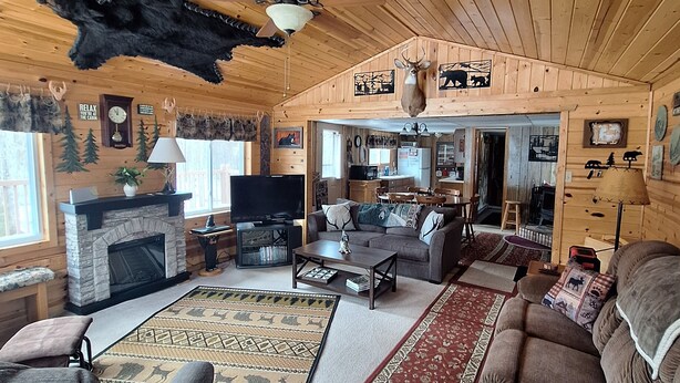L’intérieur d’un chalet en bois, avec une cheminée, un canapé, une table basse et un ventilateur de plafond.
