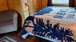 Une pièce de cabane en bois comprenant un lit, une chaise et une fenêtre.