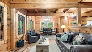 A log cabin interior with a living area featuring a sofa, a coffee table, and a dining table with chairs.