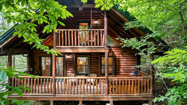 A log cabin with a two-story balcony, wooden railings, and a porch area with seating.