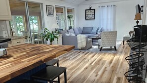 A modern kitchen with a wooden countertop and bar stools, a dining area with a sofa and chairs, and a ceiling fan. - Willsboro Relaxing Waterfront Getaway (Willsboro)