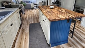 A modern kitchen with wooden flooring, a central island, and a dining area with a blue accent wall. - Willsboro Relaxing Waterfront Getaway (Willsboro)