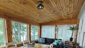 A wooden cabin interior with a dining table, white chairs, a sofa with patterned cushions, and a ceiling fan. - Willsboro Relaxing Waterfront Getaway (Willsboro)