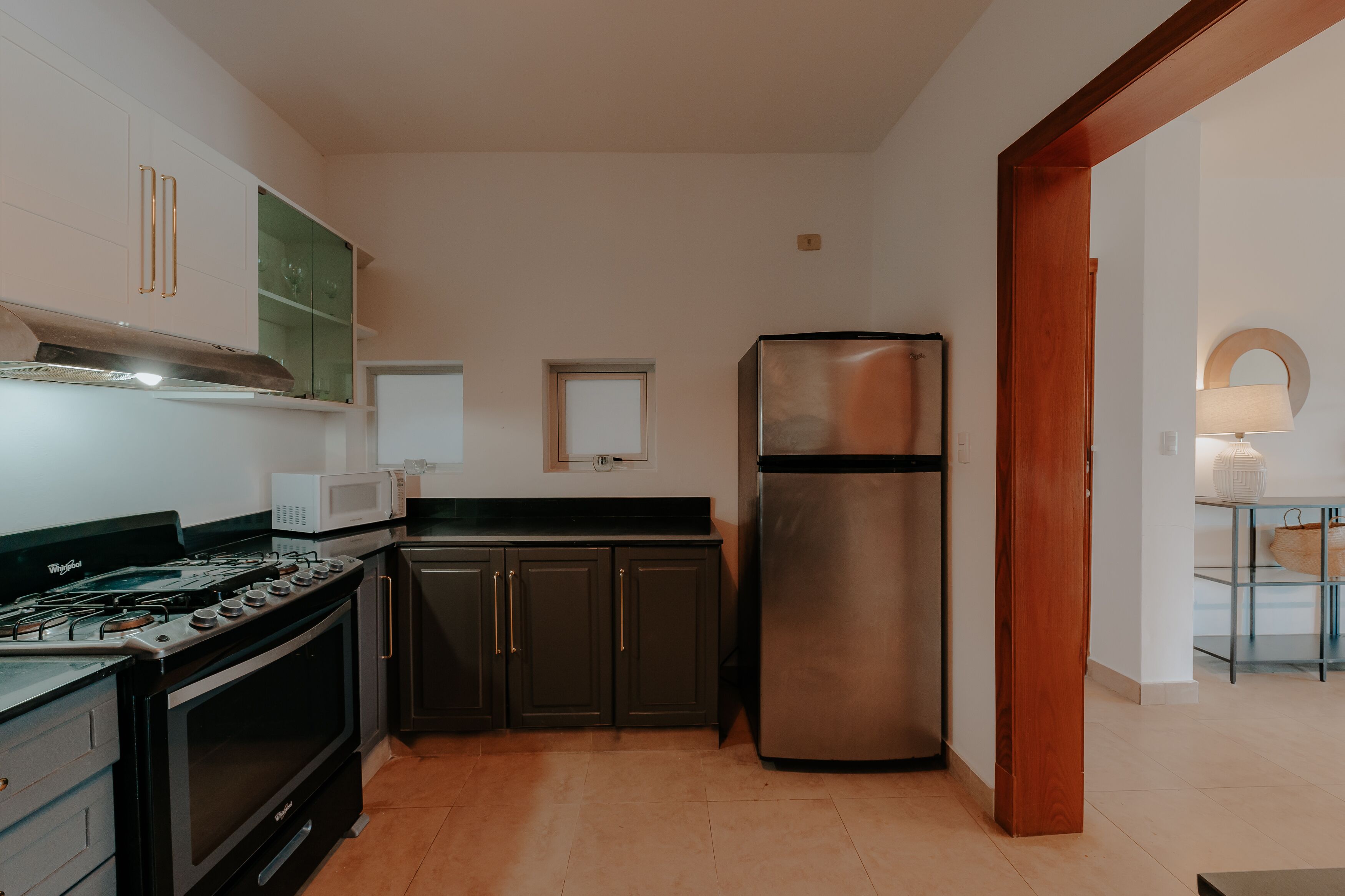 A compact kitchen with a gas stove, oven, microwave, dark cabinets, and a stainless steel refrigerator.