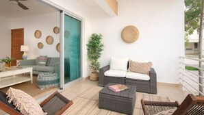 Een moderne woonkamer met een bank, salontafel en stoelen. Er is een schuifdeur naar een balkon.
