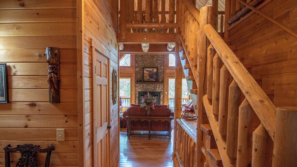 A wooden interior with a staircase, a fireplace, and a sofa in the background. - Crazy Like a Fox Log Cabin | 2 Huge Decks w/ Incredible Views | Pool Table & Foosball (Sparta)