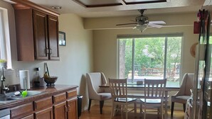 Una cucina moderna con mobili in legno, un'area pranzo con sedie bianche e un'ampia finestra che offre vista sull'esterno.