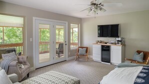 A spacious room with a sliding glass door leading to a deck, a ceiling fan, a kitchenette with a microwave, and a flat-screen TV.