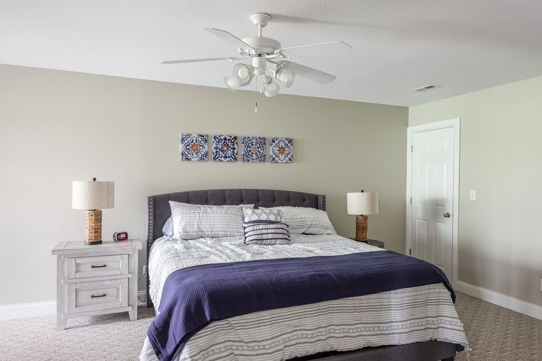 Une chambre à coucher comprenant un lit, des tables de chevet, un ventilateur de plafond et des œuvres d’art décoratives accrochées au mur.