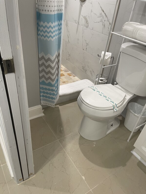 A bathroom with a toilet, a shower area, and a tiled floor.