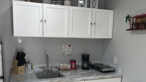 Una cucina con mobili bianchi, un piano di lavoro in marmo, un lavello e una macchina da caffè.